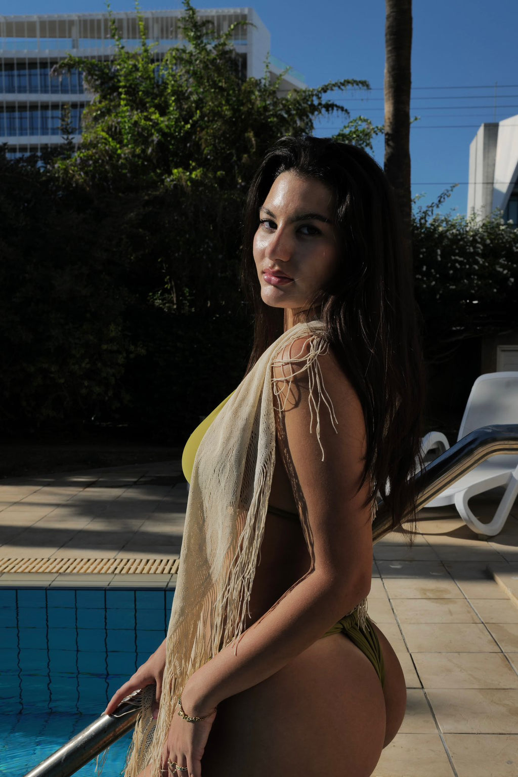 Woman in a bikini and cover-up standing by a poolside.
